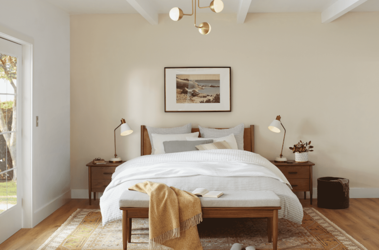 A light and airy bedroom with white and gray bedding, medium brown wood floors and a light yellow accent wall.