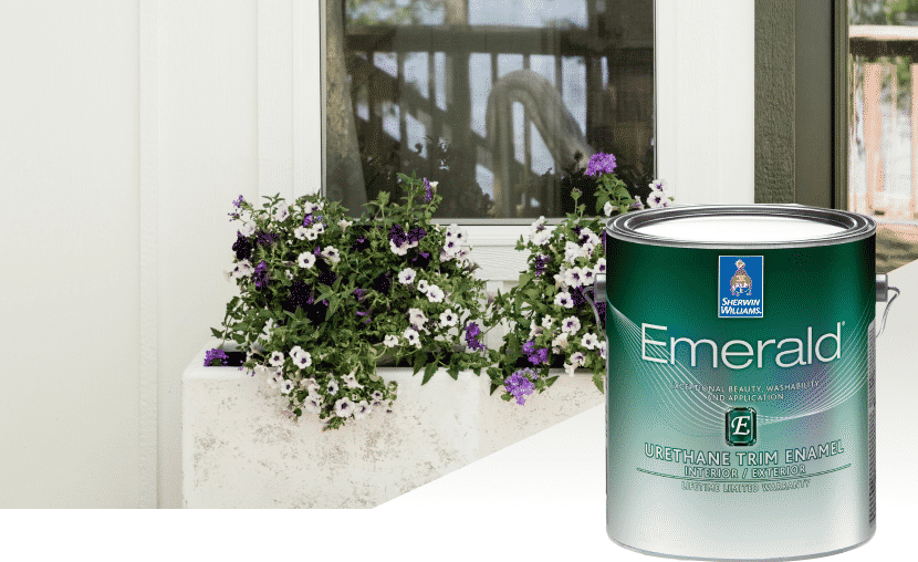 A can of Emerald Urethane Trim Enamel with a house's exterior and a concrete planter of purple and white flowers.