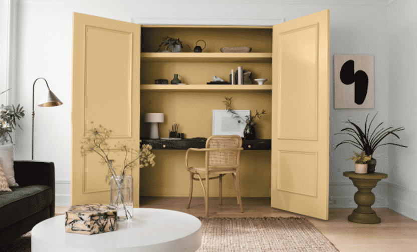 A home office with a desk built into a closet with its doors and walls painted a soft yellow.