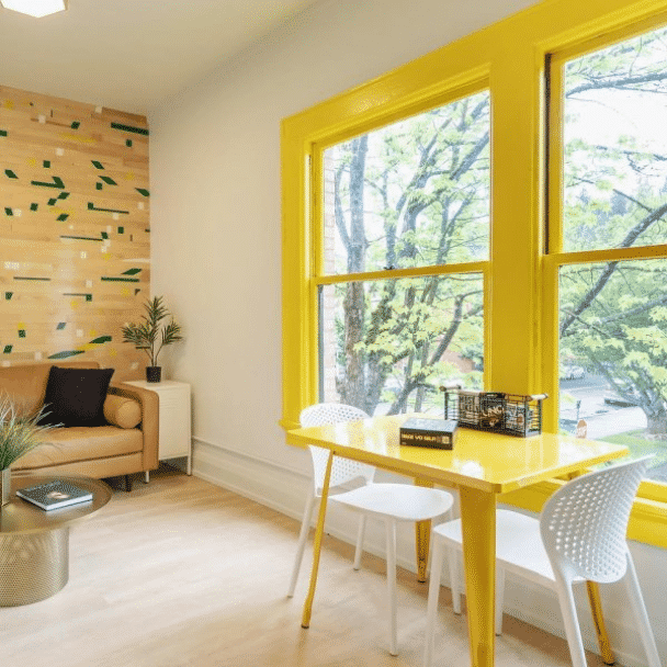 A room with bright yellow trim around large windows with a modern style bright yellow table and two white chairs in front. Photo credit to @the505eugene.